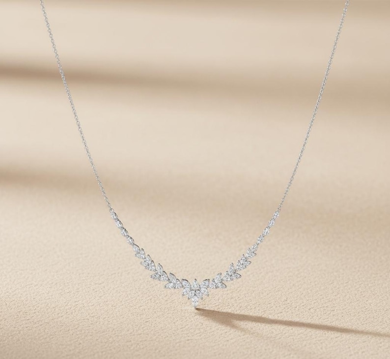 Puede incluir: Un delicado collar de plata con un dise&ntilde;o floral. El collar presenta una serie de peque&ntilde;as piedras brillantes dispuestas en un patr&oacute;n curvo, con un grupo central de piedras que forman un colgante. La cadena es fina y elegante.