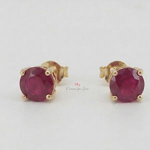 Pode incluir: Um par de brincos de ouro com tachas, cada um com uma pedra preciosa redonda de cor vermelha escura. Os brincos são definidos em uma configuração clássica de quatro pontas.