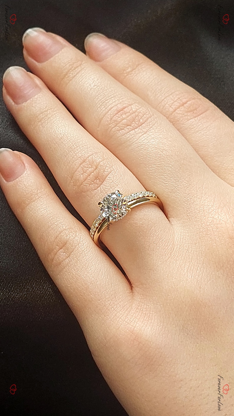 May include: A gold engagement ring set with a large, round, clear diamond center stone. The ring is set with smaller diamonds on the band. The ring is on a person's finger.
