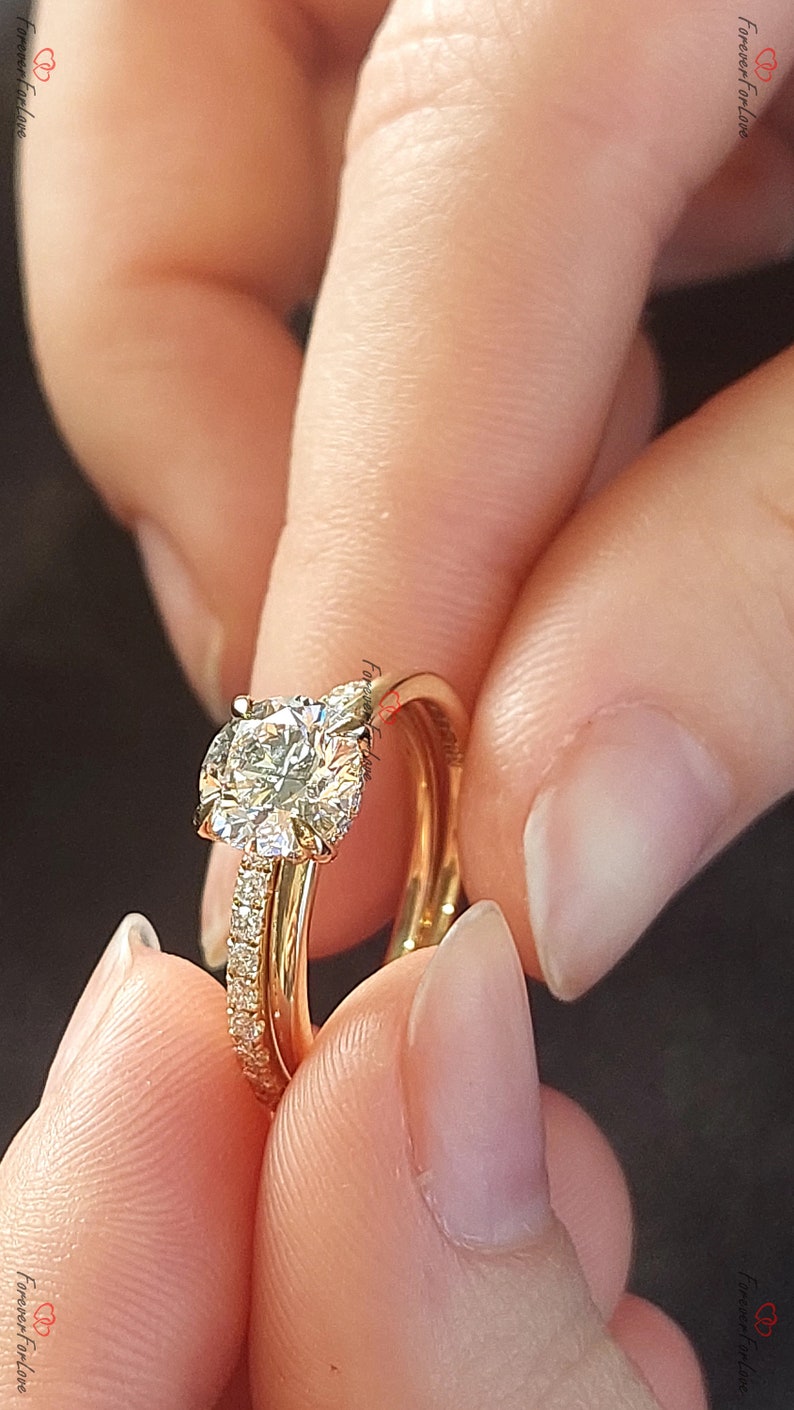 May include: A gold engagement ring with a large, round, clear diamond center stone and a smaller band of diamonds set in a pave setting. The ring is worn on a finger with a gold wedding band.