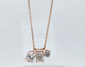 May include: Rose gold necklace with three diamond pendants: a pear-cut, a rectangular, and a round stone. The chain and settings have a warm, metallic tone, creating a delicate and elegant jewellery piece.
