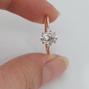 Op de afbeelding: Roségouden ring met een ovaal geslepen diamant als middensteen, geflankeerd door kleinere accentdiamanten. De band van de ring is van delicaat roségoud, en de diamanten schitteren. Een klassiek en elegant sieraad, ideaal voor verlovingen.