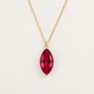 May include: A gold chain necklace featuring a marquise-cut, deep pink gemstone pendant. The faceted stone is set in a simple gold frame, suspended from a delicate gold link chain that hangs in a classic V-shape against the plain background.
