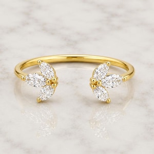Puede incluir: Un anillo abierto de oro con dos grupos simétricos en forma de hoja, cada uno engastado con tres piedras claras de talla marquesa. La banda es de oro pulido y el diseño crea un espacio en el centro, mostrando una apariencia delicada y refinada.