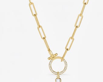 Puede incluir: Un collar dorado con una cadena de eslabones alargados. El collar presenta un colgante circular incrustado con pequeñas piedras transparentes y un colgante de gema transparente facetada colgante. El cierre es un cierre de palanca decorativo dorado.