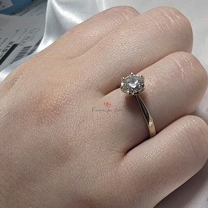May include: A gold band engagement ring with a round, clear center stone and smaller stones surrounding it.