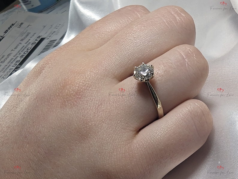 May include: A gold band engagement ring with a round, clear center stone and smaller stones surrounding it.