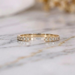 May include: A gold-colored ring with a split shank design. The ring is encrusted with small, clear gemstones along the band. The ring is set against a marble surface, creating a luxurious aesthetic. This ring is a piece of fine jewelry.