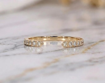 Könnte beinhalten: Ein goldfarbener Ring mit geteiltem Schaft-Design. Der Ring ist mit kleinen, klaren Edelsteinen entlang des Bandes besetzt. Der Ring ist auf einer Marmoroberfläche platziert, was eine luxuriöse Ästhetik erzeugt. Dieser Ring ist ein feines Schmuckstück.