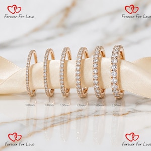 Könnte beinhalten: Sechs Ewigkeitsringe aus Roségold mit runden weißen Steinen, sortiert nach Breite von 1,00 mm bis 2,50 mm. Die Ringe liegen auf einem cremefarbenen Band. Der Text Forever For Love und Herzsymbole sind in den Ecken des Bildes zu sehen.