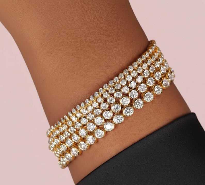 Puede incluir: Un brazalete de oro con m&uacute;ltiples filas de piedras preciosas redondas y transparentes. El brazalete est&aacute; engarzado en una banda de oro y se lleva en la mu&ntilde;eca. El fondo es de color rosa claro.