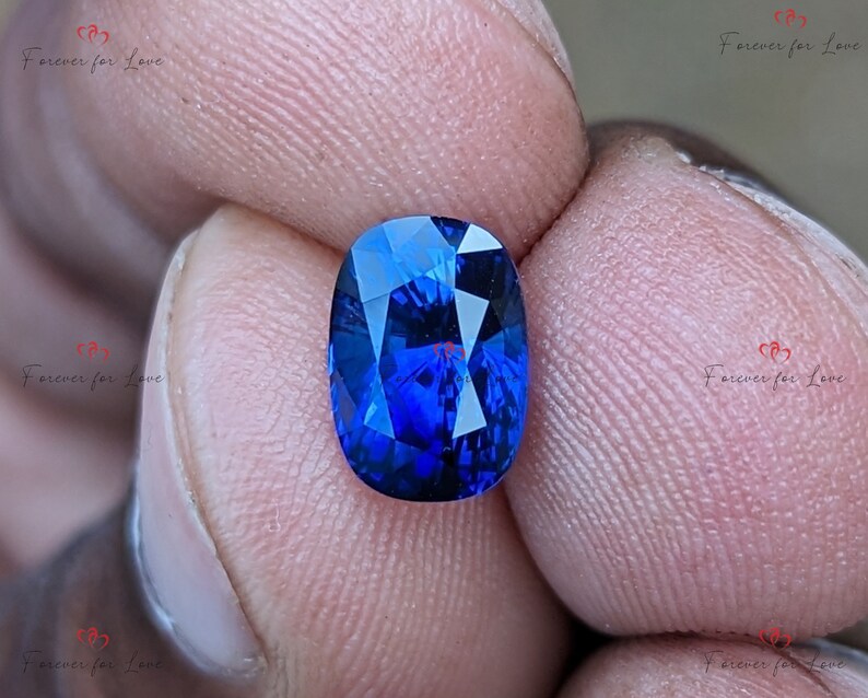 May include: A vibrant blue oval-shaped gemstone with a faceted cut. The gemstone is held between two fingers.
