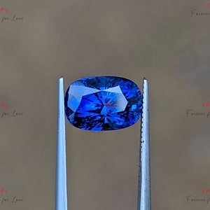 May include: A deep blue oval-shaped gemstone held by tweezers. The gemstone has a faceted cut and a brilliant shine.