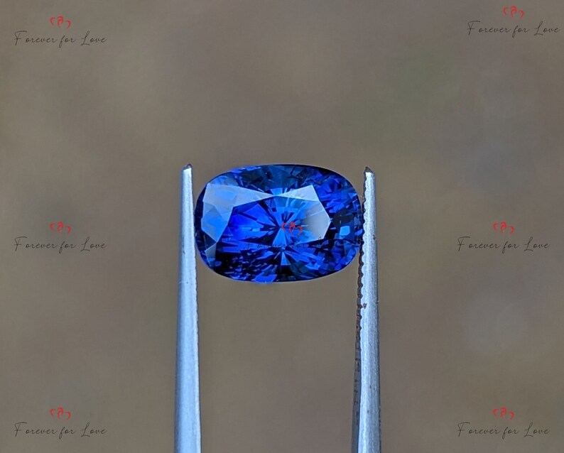 May include: A deep blue oval-shaped gemstone held by tweezers. The gemstone has a faceted cut and a brilliant shine.