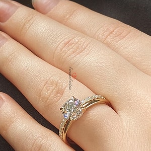May include: A gold engagement ring with a large, round, clear diamond center stone and smaller diamonds set in a pave band. The ring is on a finger.