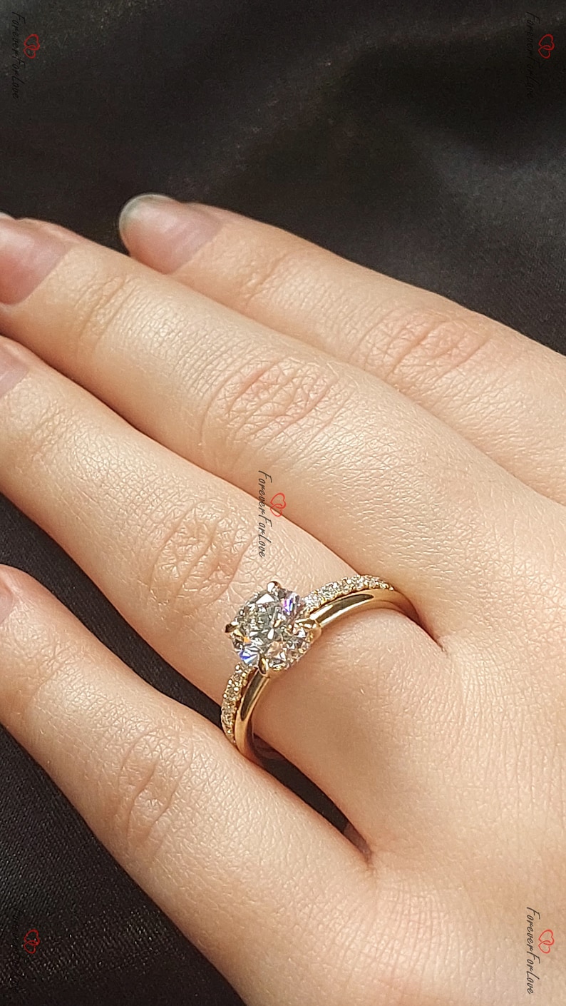 May include: A gold engagement ring with a large, round, clear diamond center stone and smaller diamonds set in a pave band. The ring is on a finger.