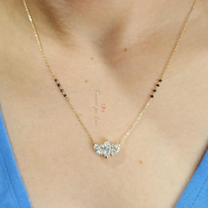 May include: A gold chain necklace with a pendant featuring five clear pear-shaped stones. The chain has black beads on one side.