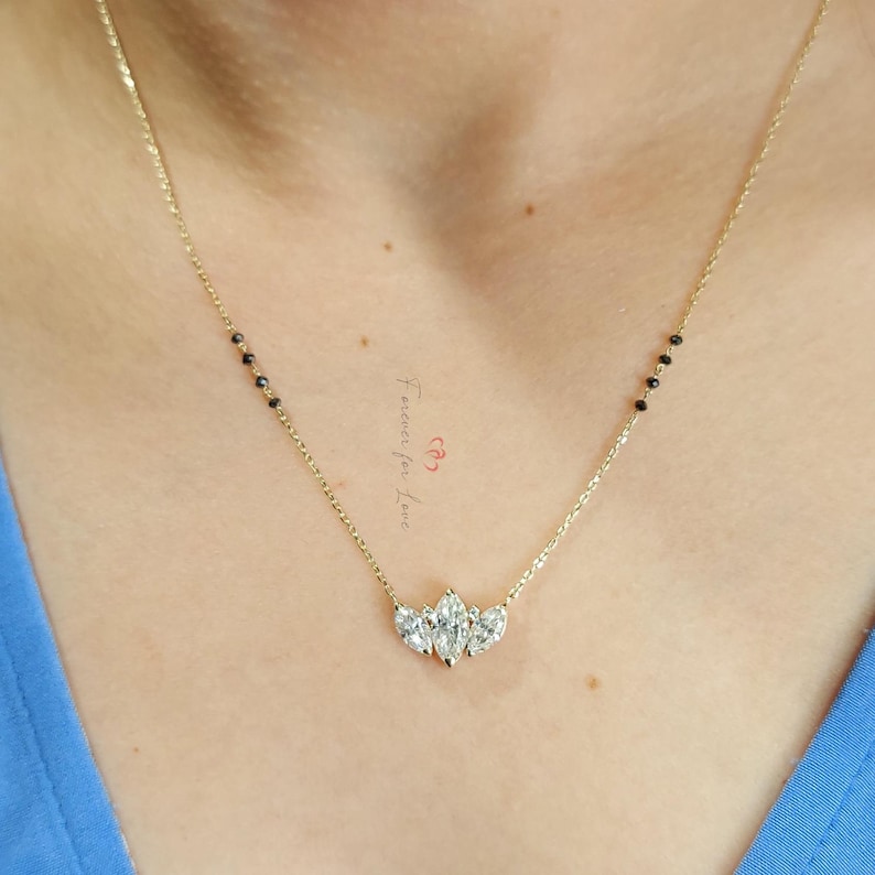 May include: A gold chain necklace with a pendant featuring five clear pear-shaped stones. The chain has black beads on one side.