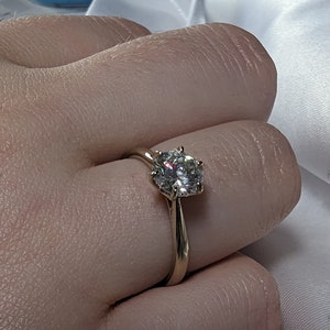May include: A gold engagement ring with a large, round, clear diamond.