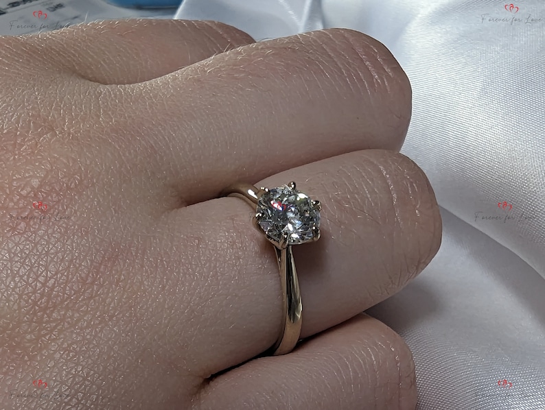 May include: A gold engagement ring with a large, round, clear diamond.
