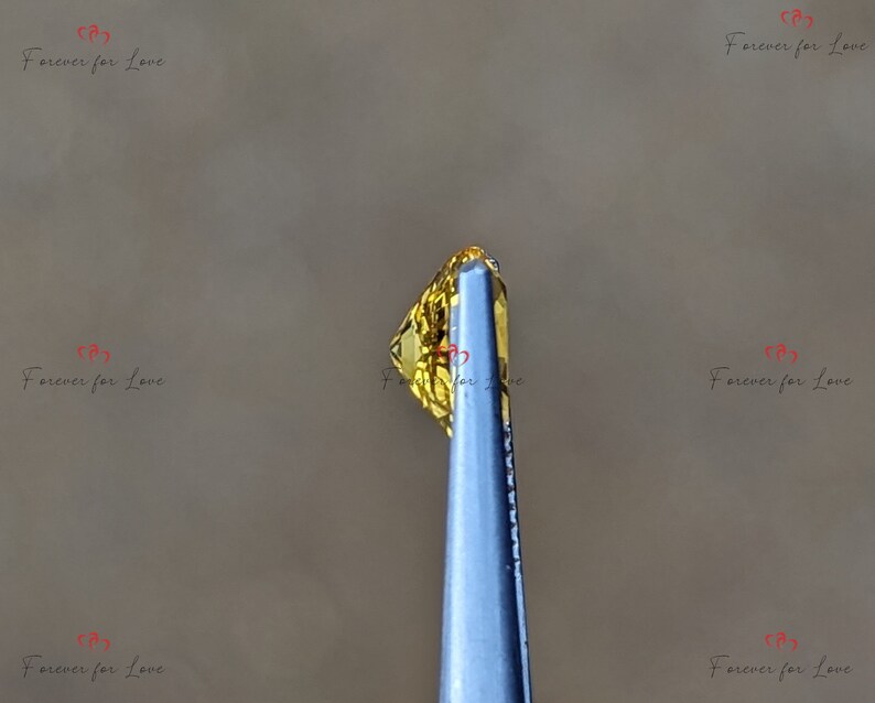 May include: A close-up of a yellow gemstone held by tweezers. The gemstone is faceted and has a golden hue.