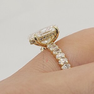 May include: A gold ring with a large, clear, oval-cut stone as the centerpiece. The ring features a halo of smaller stones around the main stone and a band adorned with additional small stones. The ring is set against a neutral background.