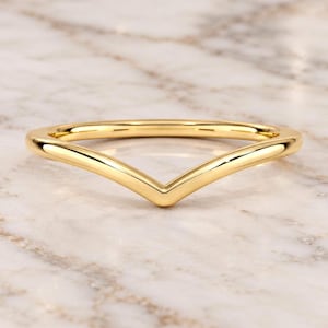 May include: A polished yellow gold ring featuring a V-shaped chevron design. The band has a smooth, rounded profile and a continuous metallic finish, creating a simple and clean aesthetic for this piece of jewellery that sits in a pointed shape.