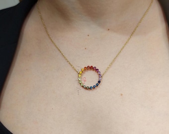 May include: A gold chain necklace with a rainbow circle pendant made of small gemstones. The pendant is a circle of colorful stones, including red, orange, yellow, green, blue, and purple.