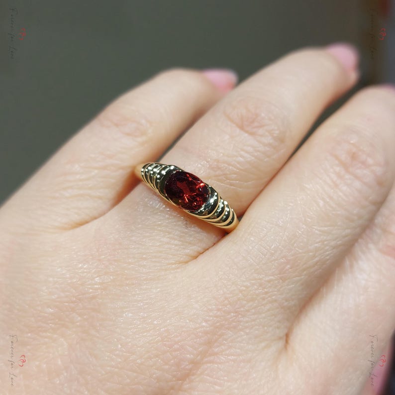 Puede incluir: Un anillo de oro con una llamativa gema roja ovalada. El anillo tiene un dise&ntilde;o acanalado en la banda, agregando textura y detalles. La gema es el punto focal, engastada en un estilo cl&aacute;sico y elegante.
