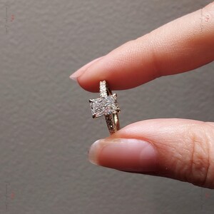 May include: A gold engagement ring with a large, square-shaped diamond in the center. The band is set with smaller diamonds.