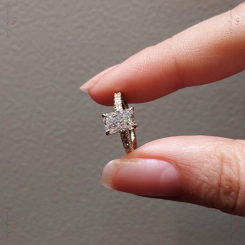 May include: A gold engagement ring with a large, square-shaped diamond in the center. The band is set with smaller diamonds.