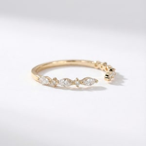 Könnte beinhalten: Ein zarter Goldring mit einer Reihe von Diamanten im Marquiseschliff und kleinen runden Diamanten. Das offene Design des Rings ermöglicht eine verstellbare Passform. Der Ring ist vor einem weißen Hintergrund platziert, um das Funkeln der Diamanten hervorzuheben.