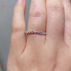 Puede incluir: Una fina banda de plata con una fila de pequeños diamantes transparentes engastados en pavé.
