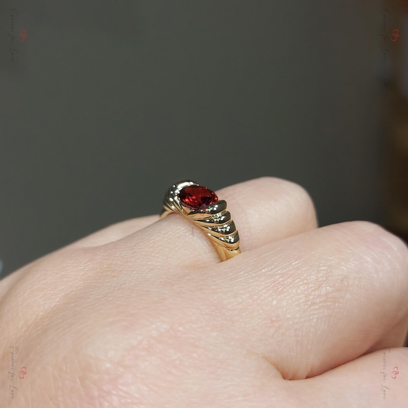 Puede incluir: Un anillo de oro con una gran gema roja ovalada. El anillo tiene una banda texturizada con peque&ntilde;as piedras de acento. El dise&ntilde;o es elegante y cl&aacute;sico, adecuado para ocasiones especiales.
