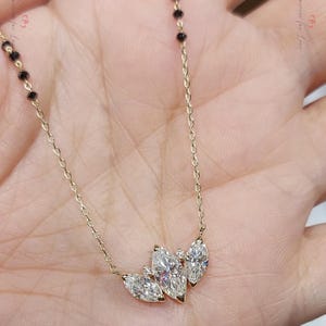 May include: A gold chain necklace with a pendant featuring three marquise-shaped diamonds. The diamonds are set in a prong setting and are surrounded by smaller diamonds.