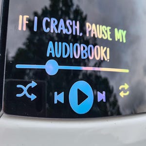May include: A holographic sticker with the text "IF I CRASH, PAUSE MY AUDIOBOOK!" and a media player interface. The design includes play, pause, skip, and shuffle icons, all in a gradient of colors.