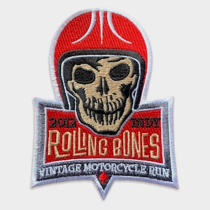 May include: Red, white and grey embroidered patch featuring a skull wearing a helmet and the text "2012 Indy Rolling Bones Vintage Motorcycle Run".