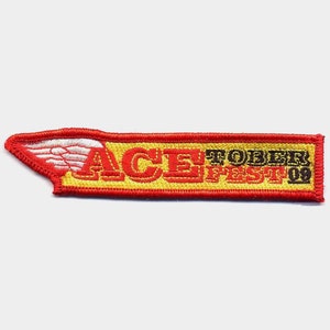 May include: Red and yellow embroidered patch with a white wing design and the text "ACE! TOBER FEST '09".