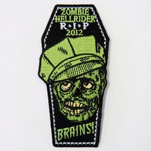 May include: A black and green embroidered patch shaped like a coffin with the text "Zombie Hellrider R*I*P 2012" and "Brains!"  The patch features a cartoon zombie with a green face and a green cap.
