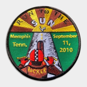 May include: An embroidered patch in green, brown and yellow with the text "Run to the Sun" and "Memphis Tenn., September 11, 2010". The patch features a cartoon illustration of a person riding a motorcycle towards a bright sun.