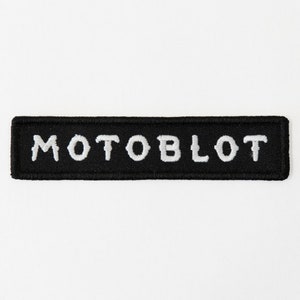 Op de afbeelding: Zwart-wit geborduurde patch met het woord "MOTOBLOT" in witte letters.