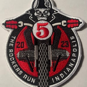 May include: A black and white embroidered patch with a red background. The patch features a skeleton riding a motorcycle with the number "5" on the front. The text "The Rockers Run 2023 Indianapolis" is around the edge of the patch.