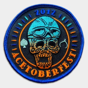 May include: A black and orange embroidered patch featuring a skull wearing a blue helmet and goggles. The text "2012 ACTOBERFEST" surrounds the skull.