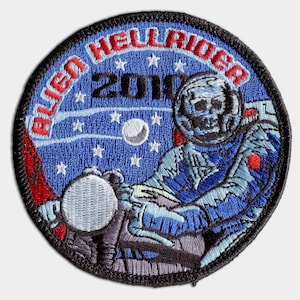 May include: A blue and red embroidered patch with a skull-faced astronaut riding a motorcycle in space. The patch says "Alien Hellrider 2010" around the edge.