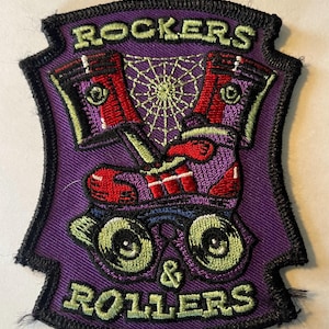 Peut inclure: Patch brodé violet avec une paire de patins à roulettes et le texte "ROCKERS & ROLLERS" en lettres vertes et blanches.