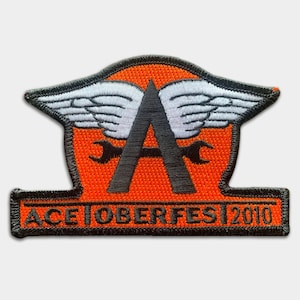 May include: Orange and black embroidered patch with a winged letter A and the text "ACETOBERFEST 2010".