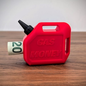 May include: A bright red plastic container shaped like a miniature fuel can with a black nozzle. The side of the container features the embossed text GAS MONEY. A rolled-up twenty-pound note is inserted into the side opening of the container.