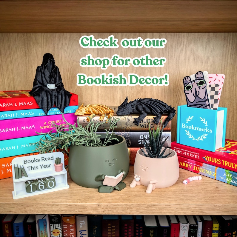 Peut inclure: Une &eacute;tag&egrave;re en bois pr&eacute;sente des d&eacute;corations sur le th&egrave;me des livres. On y trouve une figurine noire de la Faucheuse, des figurines de dragons et des pots de fleurs avec des visages. Une petite &eacute;tag&egrave;re blanche indique "Livres lus cette ann&eacute;e" avec le chiffre 160.