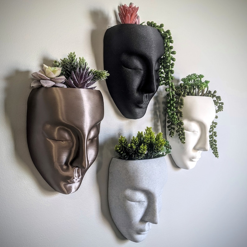 May include: Four different face-shaped planters with succulents. The planters are made of ceramic and have a matte finish. The succulents are green and have a variety of textures.