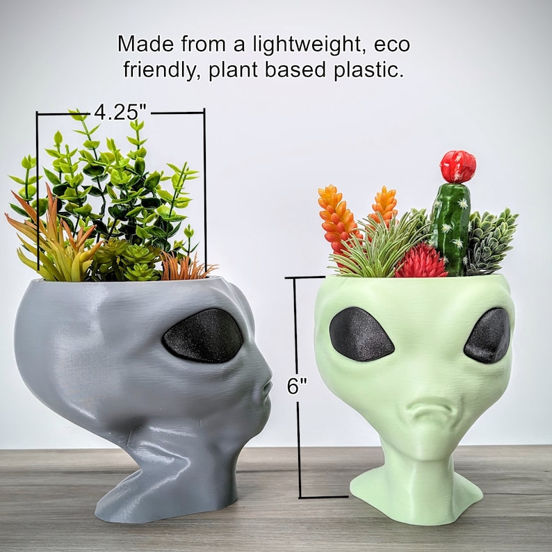May include: Two alien head planters, one gray and one green, each holding a small succulent arrangement. The gray planter is 4.25 inches tall and the green planter is 6 inches tall. Made from lightweight, eco-friendly, plant-based plastic.